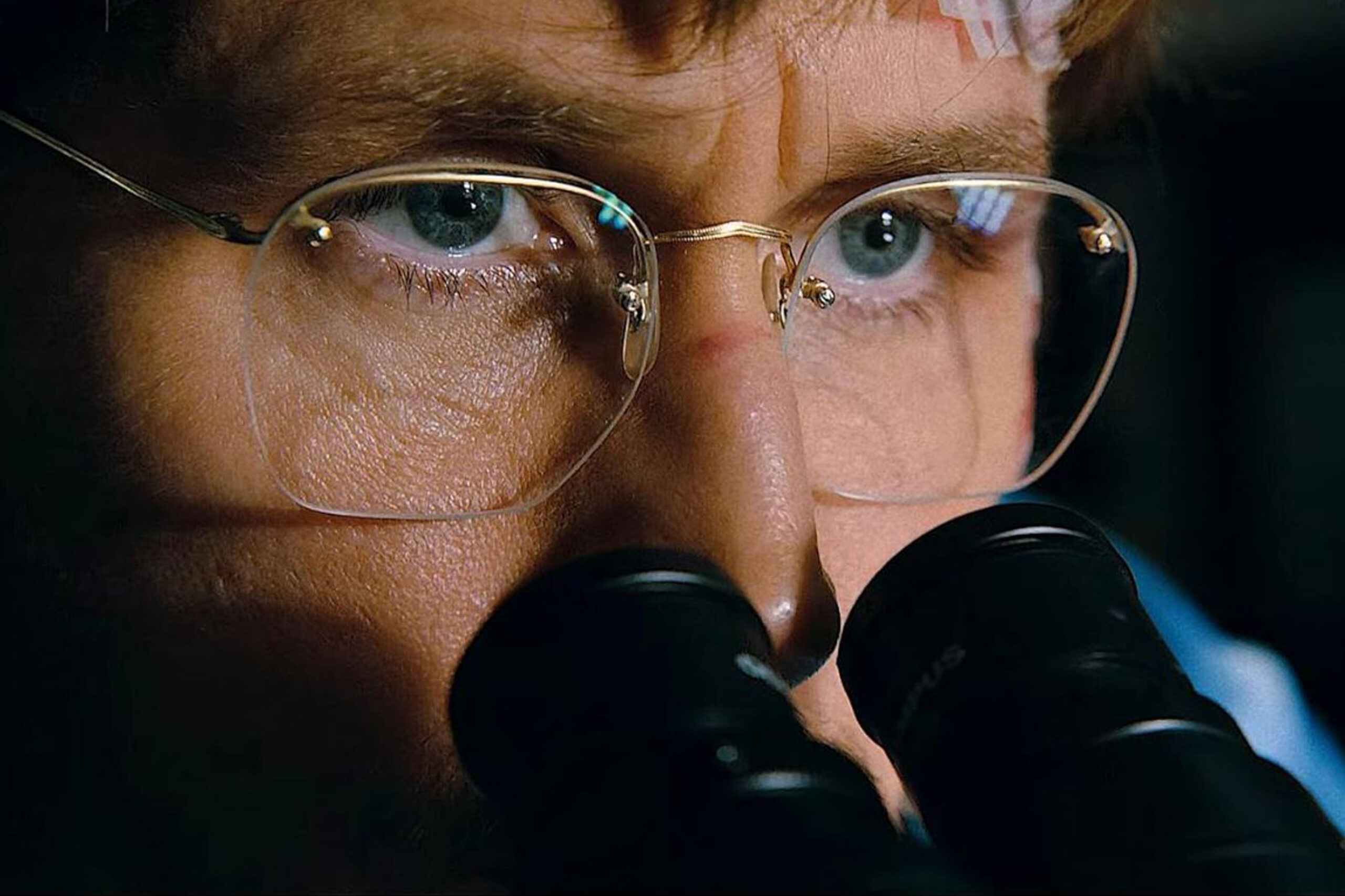 Das Bild zeigt Ryan Gosling in einer Nahaufnahme mit Brille an einem Mikroskop