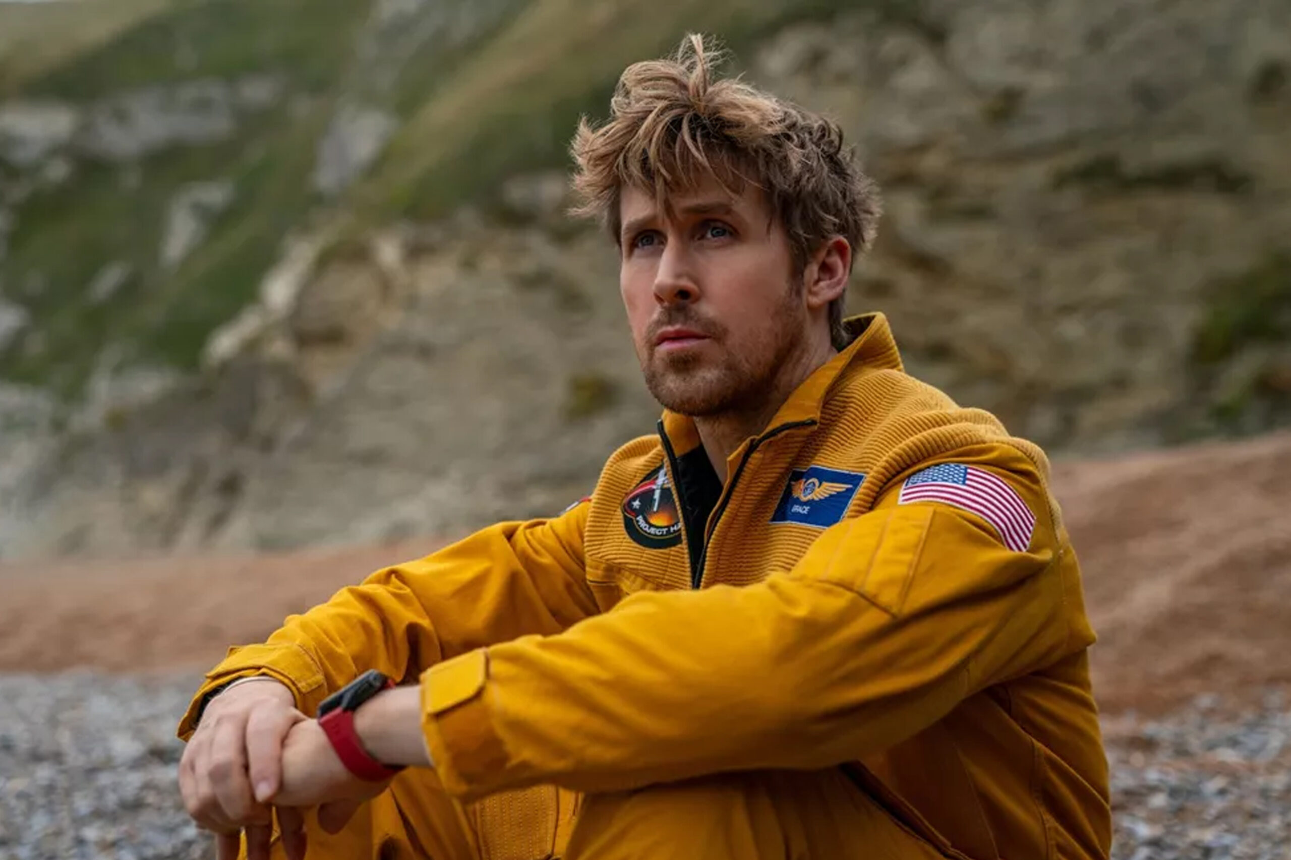 Das Bild zeigt Ryan Gosling in seiner Rolle als Ryland Grace im NASA Anzug, sitzend im Kies