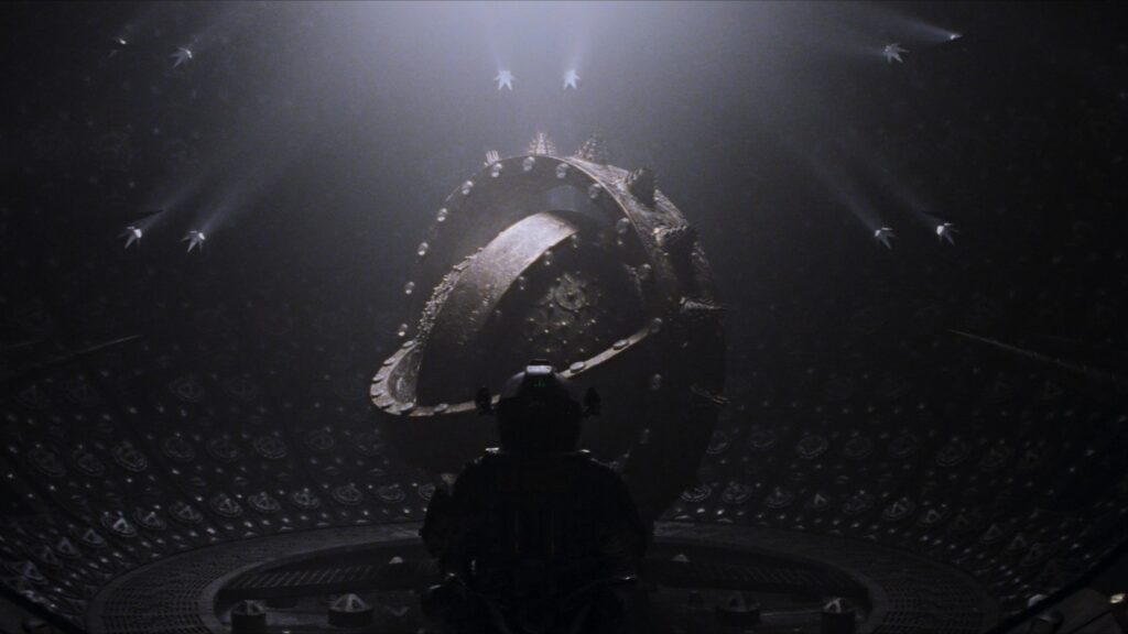 Das Bild zeigt den Antriebskern des Raumschiffs Event Horizon. Eine große Metallkugel, umgeben von metallischen Ringen, in einem großen Runden Raum. Davor sieht man die Silhouette eines Raumfahrers, der auf die Kugel blickt. | Eure 5 liebsten Raumfahrzeuge