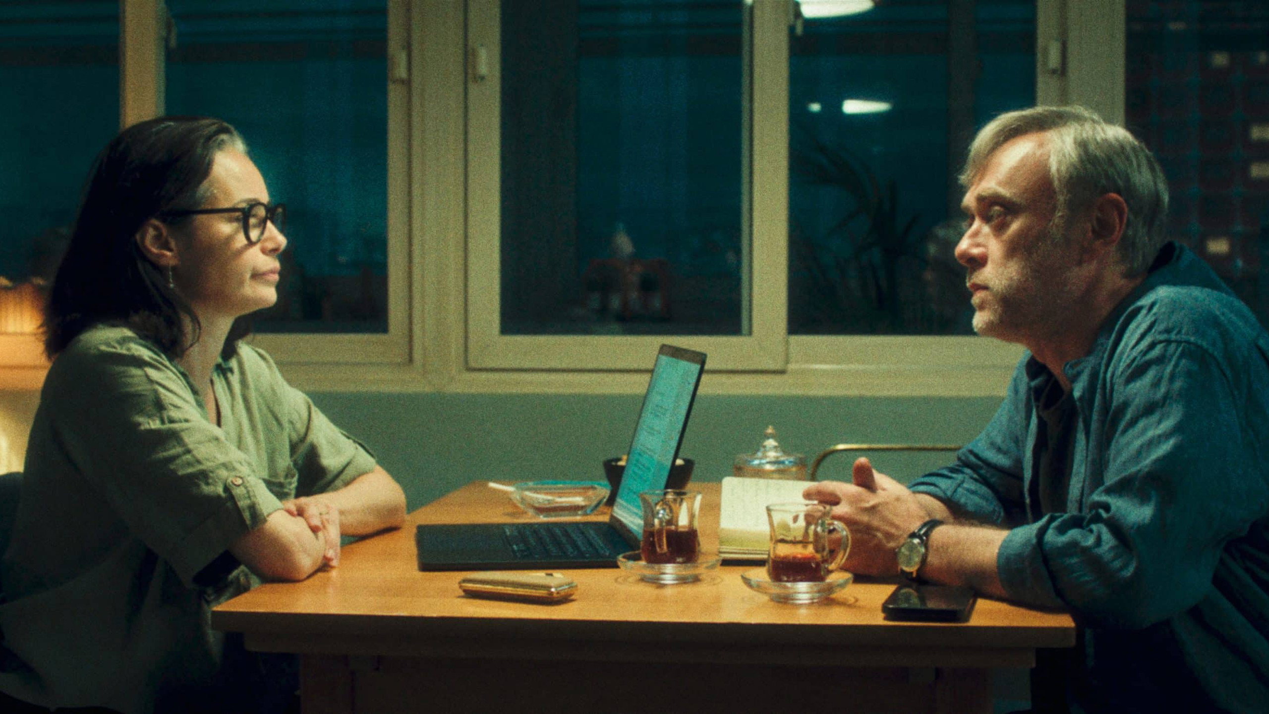 Eine Frau und ein Mann sitzen sich gegenüber. Sie hat vor sich einen geöffneten Laptop, er ein Notizbuch.