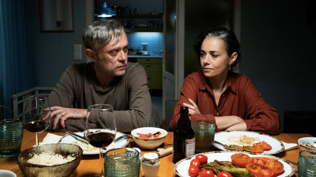 Ein Mann und eine Frau sitzen an einem Tisch mit Essen und Getränken. | Gelbe Briefe Filmkritik