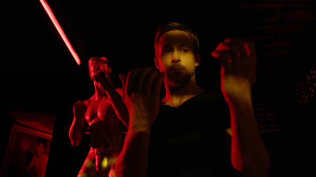 Ryan Gosling als Julian in „Only God Forgives“, stehend in einem rot-gelb beleuchteten Raum, mit erhobenen Händen vor einer kämpferischen Statue im Hintergrund; atmosphärisch düstere Neonästhetik. | Top 5 Filme die besser sind als ihr Ruf