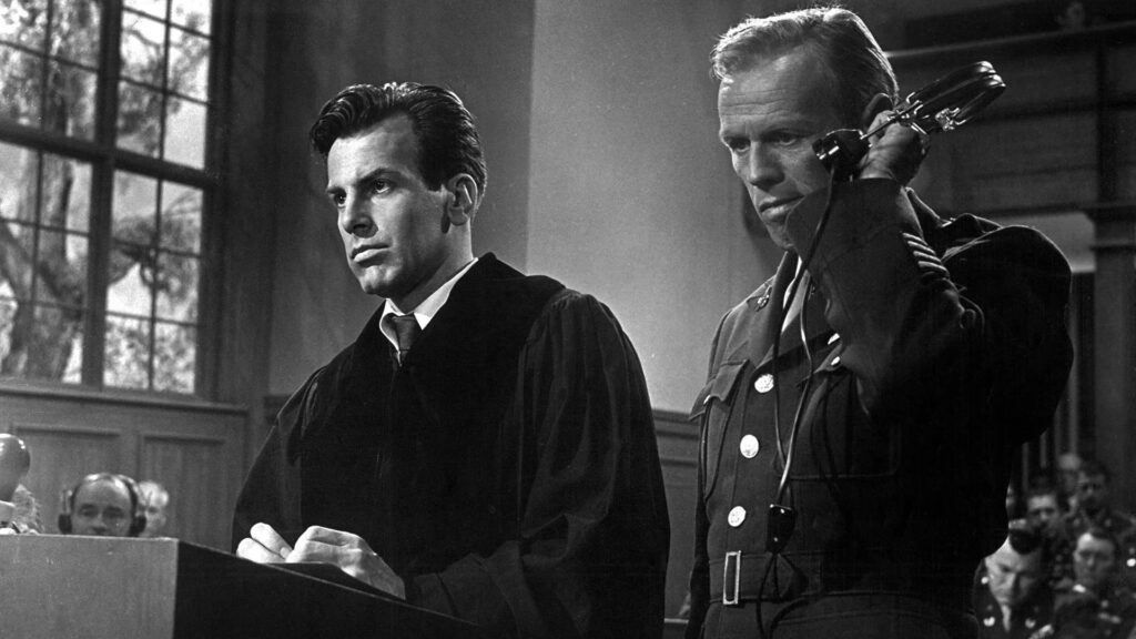 Maximilian Schell in Richterrobe und Richard Widmark in Uniform stehen in einem Gerichtssaal, Widmark hält sich einen Kopfhörer ans Ohr - Eine Szene aus "Das Urteil von Nürnberg" (1961) | Die 5 besten Justiz- und Gerichtsfilme