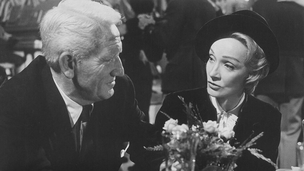 Spencer Tracy redet mit Marlene Dietrich, vor ihnen ist ein Blumengesteck in einer Vase - Eine Szene aus "Das Urteil von Nürnberg" (1961) | Die 5 besten Justiz- und Gerichtsfilme
