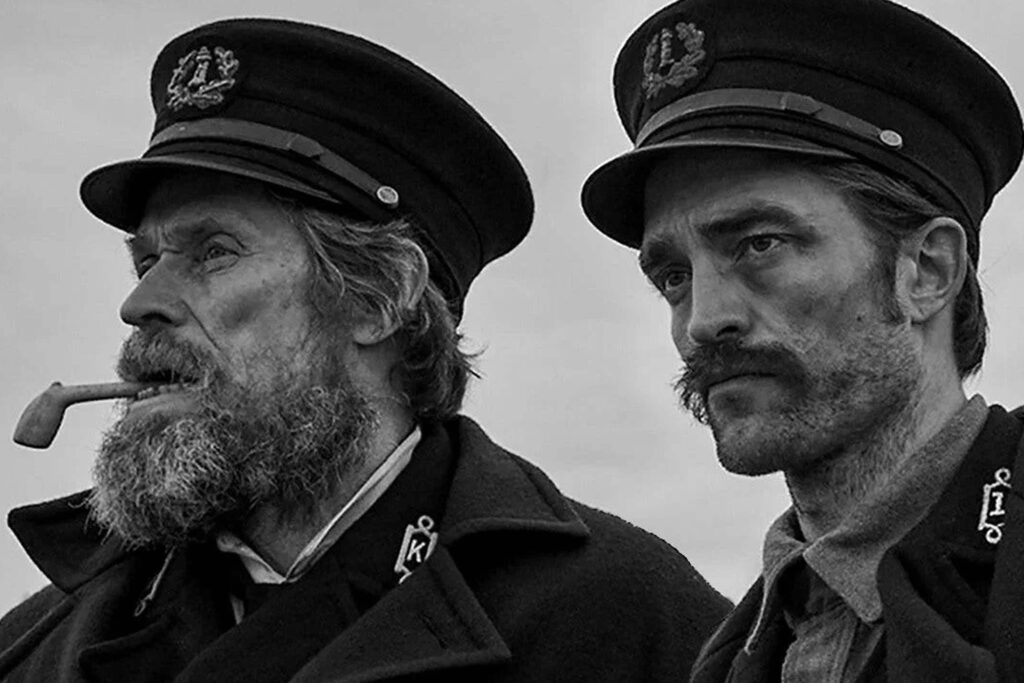 Robert Pattinson und Willem Dafoe in „Der Leuchtturm“ in einer schwarz‑weißen Aufnahme: beide in wettergegerbten Seemannsuniformen, mit Mützen und ernsten Blicken, während Dafoe eine Pfeife im Mund hält. Die Szene betont die raue, maritime Atmosphäre des Films. | Media Monday #775