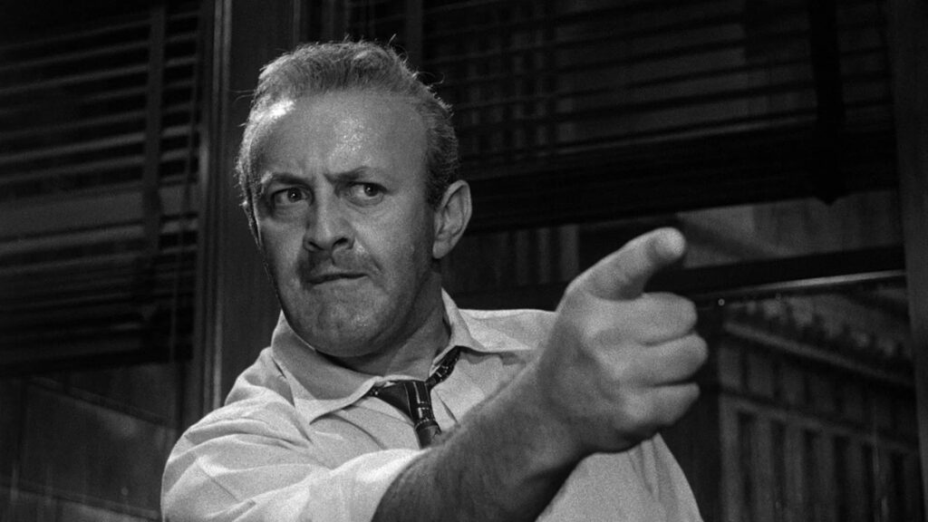 Lee Cobb zeigt mit wütendem Gesichtsausdruck auf etwas außerhalb des Bildes - Eine Szene aus "Die zwölf Geschworenen" (1957)