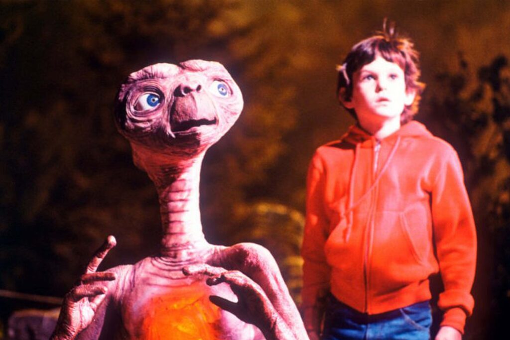 Das Bild zeigt E.T. (links) und Elliott (Henry Thomas) die beide in den Himmel auf ein grelles Licht blicken | Die 5 liebsten Aliens