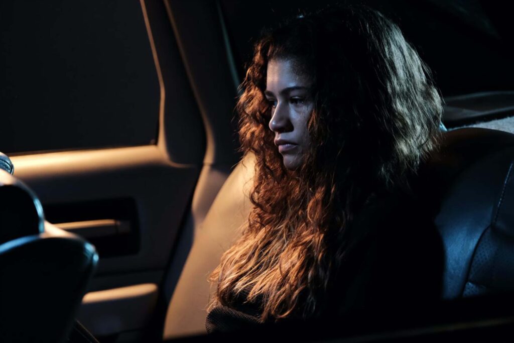 Rue Bennett (gespielt von Zendaya) aus „Euphoria“ sitzt nachdenklich auf dem Rücksitz eines Autos, in warmes Licht getaucht; eine visuelle Darstellung von Verletzlichkeit, emotionalem Druck und der düsteren Coming‑of‑Age‑Atmosphäre der Serie. | Die 5 besten Queer Cinema Serien