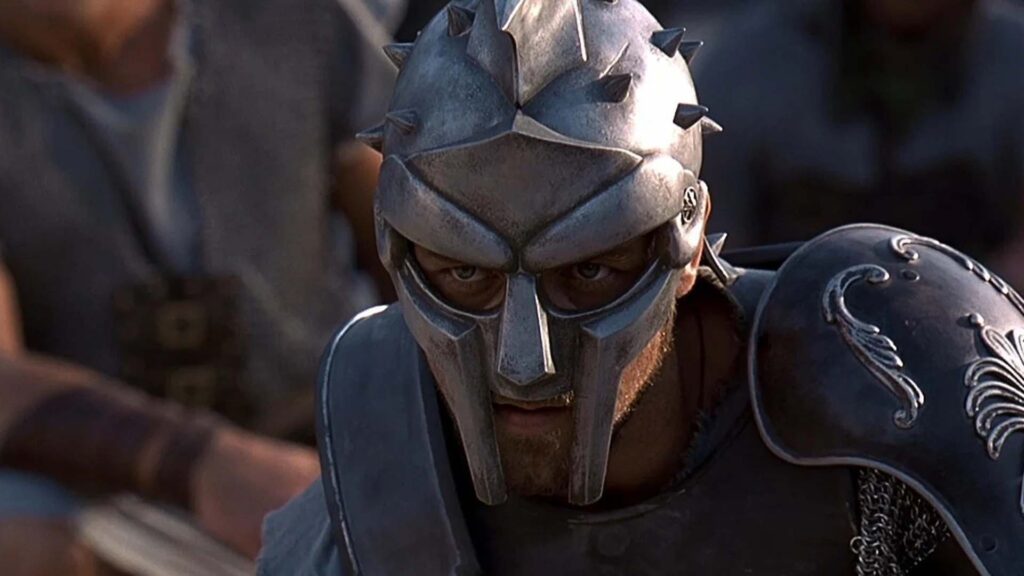 Maximus (Russell Crowe) aus „Gladiator“ in voller Gladiatorrüstung, mit metallischem Helm und Gesichtsschutz; nur seine Augen sind sichtbar. Er steht inmitten anderer Krieger, die antike Kleidung tragen — eine kraftvolle, konzentrierte Momentaufnahme kurz vor dem Kampf. | Themenübersicht Juni 2026 – Die 5 BESTEN am DONNERSTAG