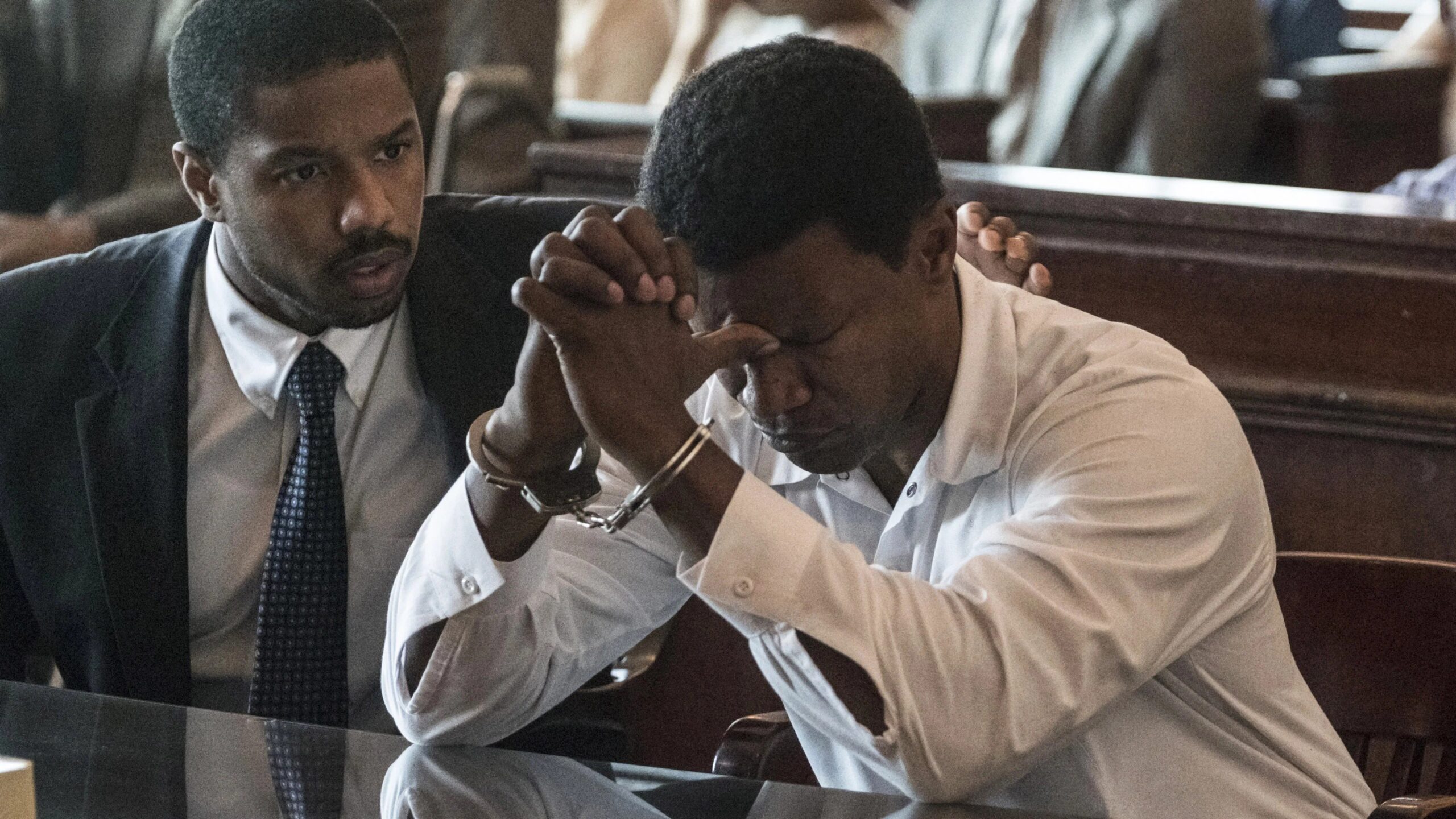 Michael B. Jordan und Jamie Foxx am Anwaltstisch, Jordan hat die Hand auf Foxxs Schulter, dieser hält verzweifelt seine Arme in Handschellen vor seinen Kopf - Eine Szene aus "Just Mercy" (2019) | Die 5 besten Justiz- und Gerichtsfilme