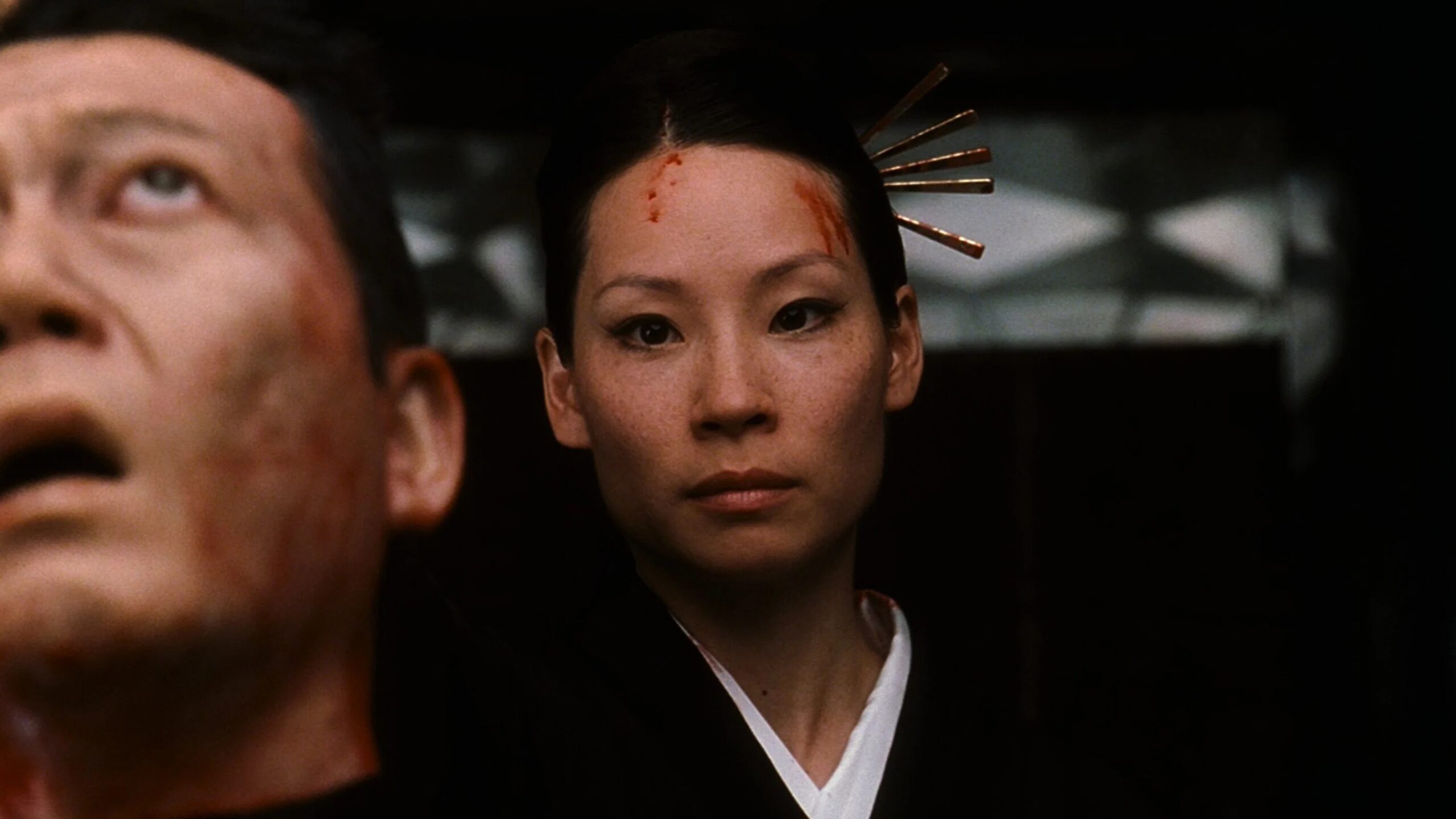 O-Ren Ishii blickt streng in die Kamera und hält einen anderen Kopf vor sich