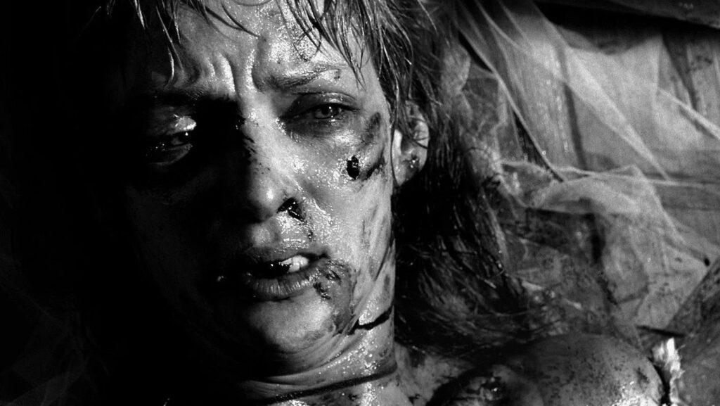 Uma Thurman liegt auf dem Boden schaut mit zerschundenem Gesicht nach oben in die Kamera, das Bild ist in Schwarz-Weiß | Kill Bill: The Whole Bloody Affair