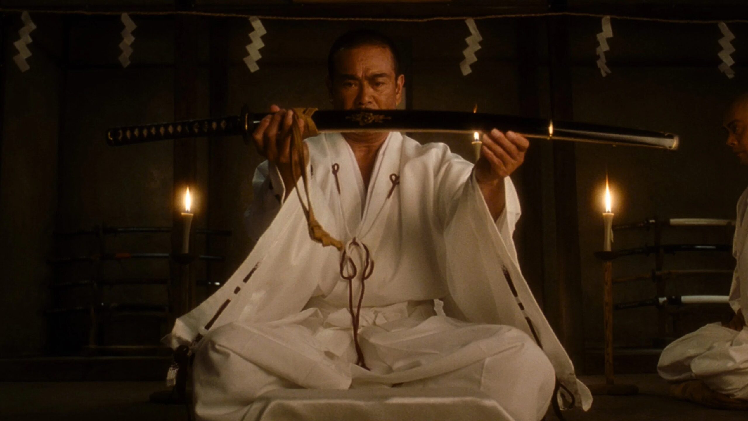 Sonny Chiba als Hattori Hanzo sitzt auf seinen Knien und hält ein Samuraischwert vor sich