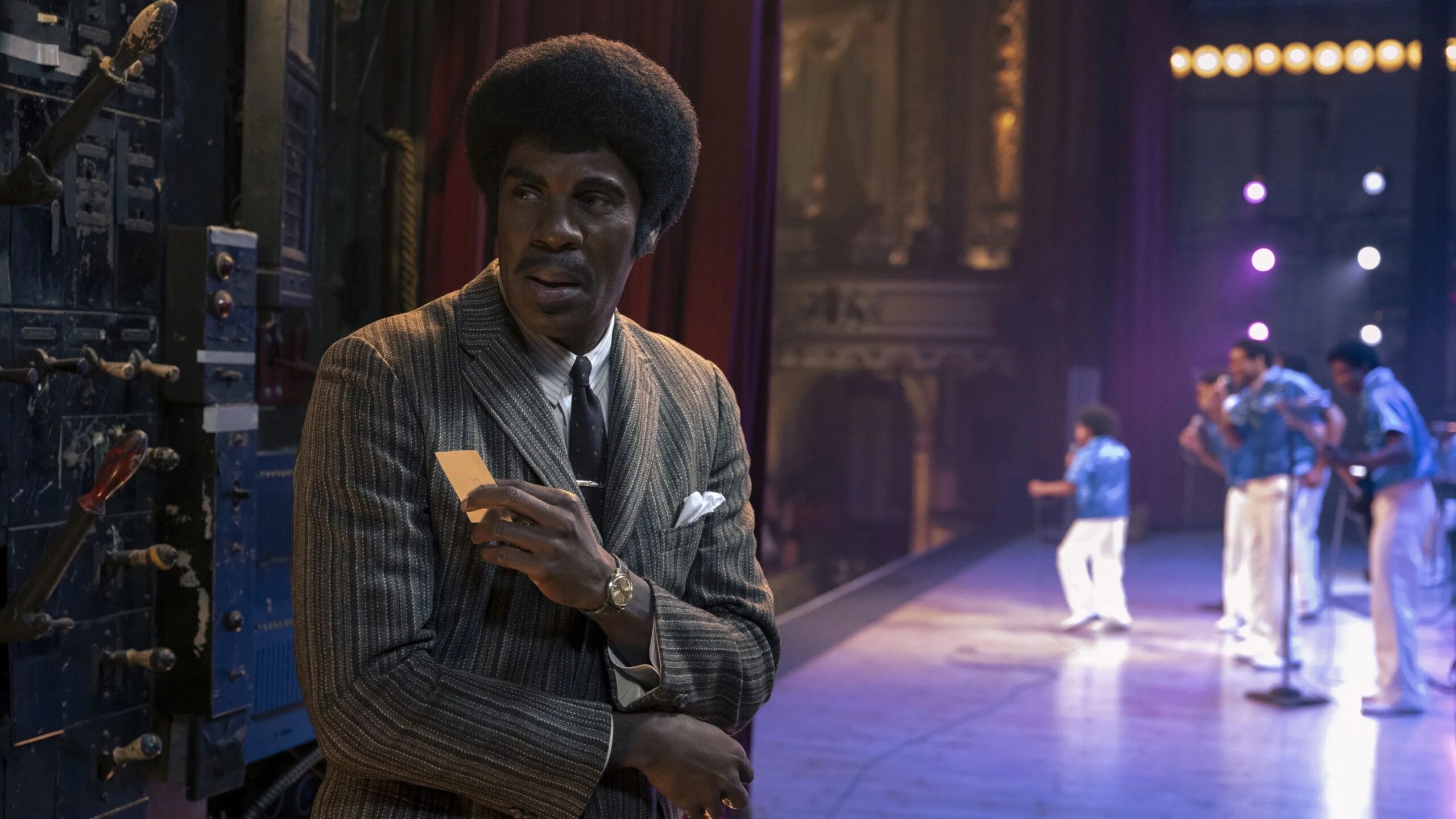 Joe Jackson (Colman Domingo) steht Backstage und hält eine Visitenkarte in der Hand, im Hintergrund sind seine Söhne auf der Bühne