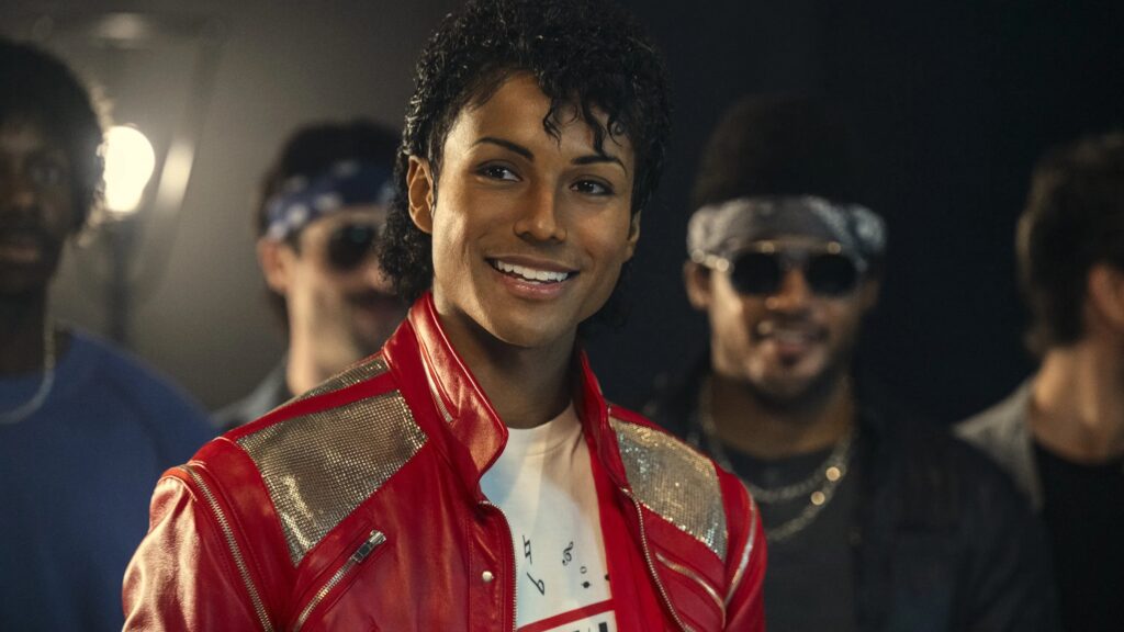 Michael (Jaafar Jackson) mit einer roten Lederjacke steht vor ein paar Gangmitgliedern und lächelt in die Kamera