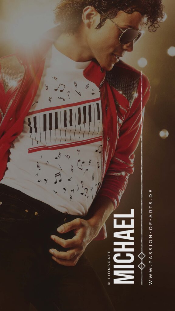 Jaafar Jackson als Michael Jackson in ikonischer roter MJ‑Jacke mit metallischen Schulterdetails und Sonnenbrille; selbstbewusste Pose vor warmen Lichtreflexen, weißes T‑Shirt mit Klaviertasten‑ und Musiknoten‑Design; dynamische, bühnenhafte Atmosphäre aus dem Film Michael (2026).