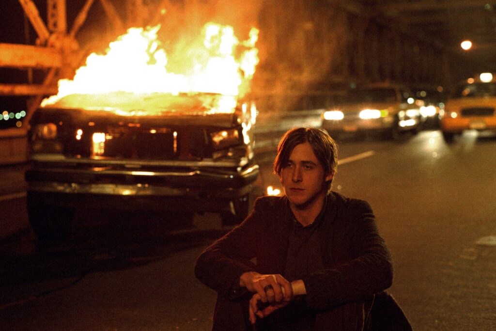 Ryan Gosling als Henry in Stay (2005), sitzt nachts auf der Straße vor einem brennenden Auto; dramatische, filmische Szene mit urbanem Chaos. | Media Monday #777