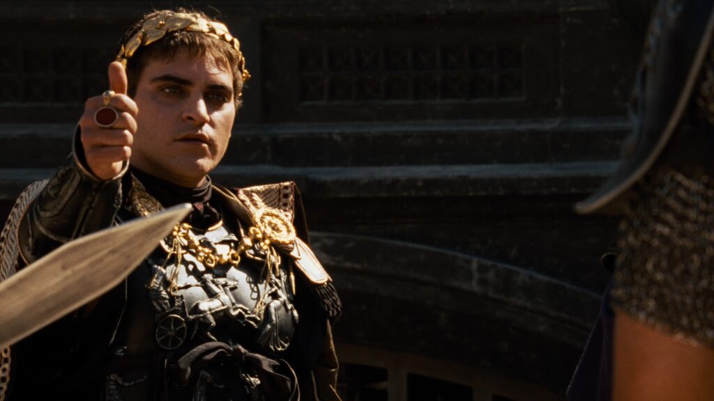 Commodus (Joaquin Phoenix) hebt seinen Daumen hoch und blick auf eine Person außerhalb des Bildes