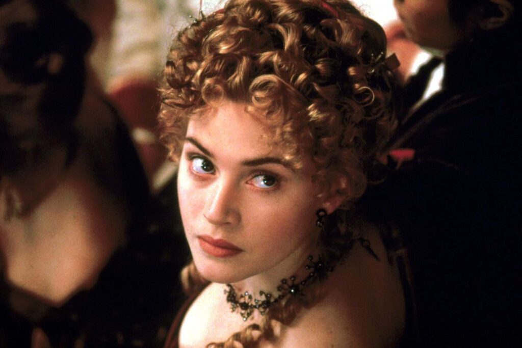 Kate Winslet als Ophelia in Kenneth Branaghs „Hamlet“ in einer eleganten Nahaufnahme; mit kunstvoll hochgesteckten blonden Locken, dunklem Schmuck und historischem Kostüm steht sie inmitten einer festlichen Gesellschaftsszene, was die opulente, dramatische Atmosphäre der Shakespeare‑Verfilmung unterstreicht. | Themenübersicht Juli 2026