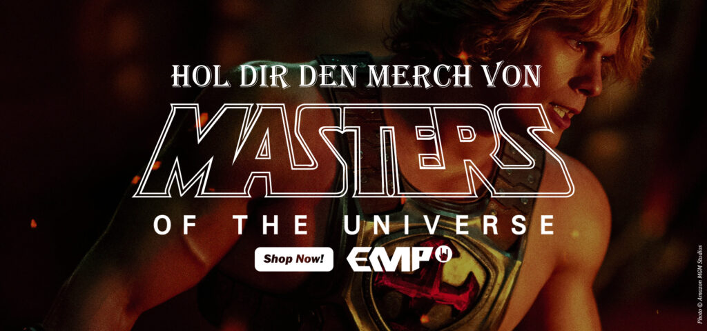 He‑Man, dargestellt von Nicholas Galitzine, steht muskulös und gerüstet vor einem dunklen Hintergrund mit glühenden Funken; darüber der Werbetext „Hol dir den Merch von Masters of the Universe – Shop Now! EMP“, unten der Hinweis „Photo © Amazon MGM Studios“.