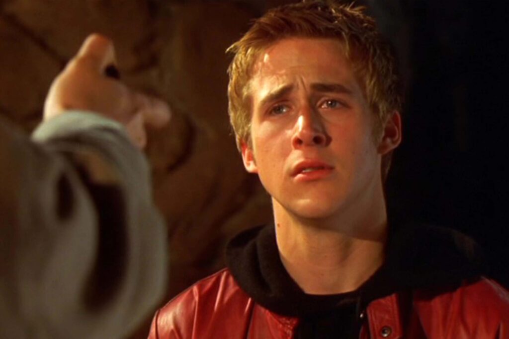 Ryan Gosling als Richard in „Mord nach Plan“ in einer intensiven Nahaufnahme. Er trägt eine rote Jacke und blickt ernst auf eine Person im Vordergrund, deren Hand ihm entgegenstreckt. Der Hintergrund ist dunkel und felsig, die Szene wirkt angespannt und konfrontativ. | Media Monday #779