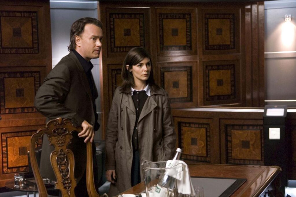 Robert Langdon (Tom Hanks) und Sophie Neveu (Audrey Tautou) stehen in einem edlen, holzvertäfelten Raum vor einem Tisch mit Gläsern und einer Flasche; die warme Beleuchtung und das formelle Interieur unterstreichen die rätselhafte, spannungsgeladene Ermittlungsatmosphäre des Thrillers „The Da Vinci Code – Sakrileg“. | Themenübersicht Juli 2026