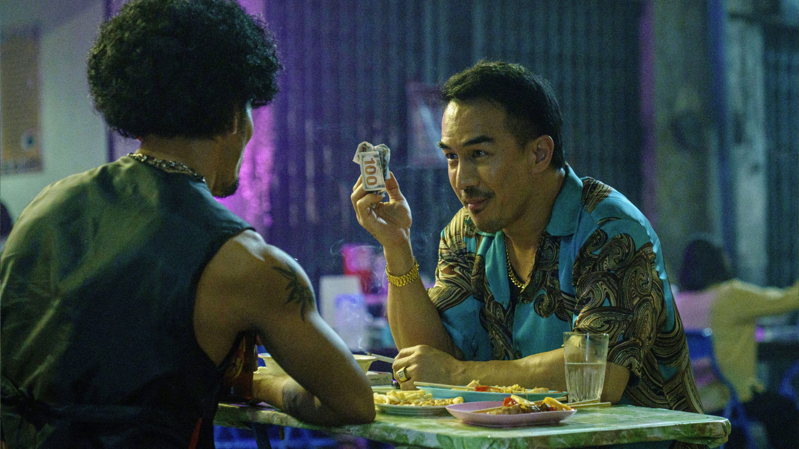 Das Bild zeigt Joe Taslim mit einem Geldschein in der Hand in einer Szene des Films The Furious.