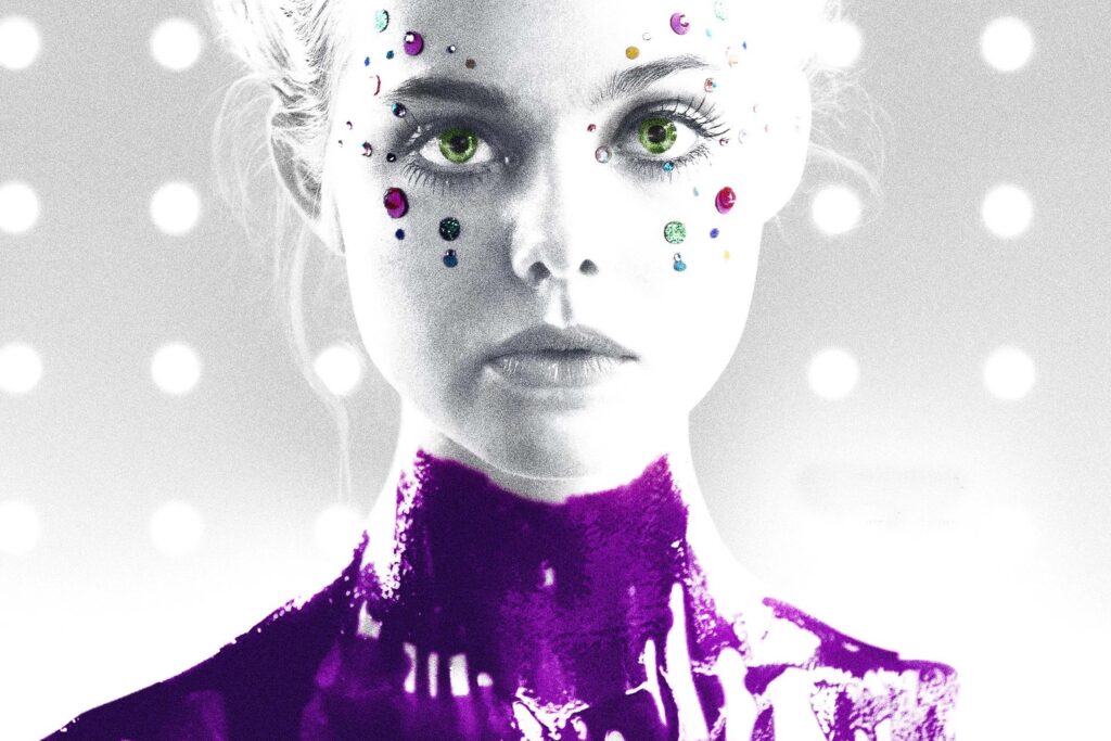 Elle Fanning als Jesse in „The Neon Demon“ in einer intensiven Nahaufnahme; das junge Model mit zurückgestylten blonden Haaren, leuchtend grünen Augen und glitzernden Gesichtsapplikationen blickt direkt in die Kamera, während eine metallisch‑violette Textur ihren Hals bedeckt und ein futuristisch beleuchteter Hintergrund die kühle, surreal‑bedrohliche Ästhetik des Films betont. | Themenübersicht Juli 2026