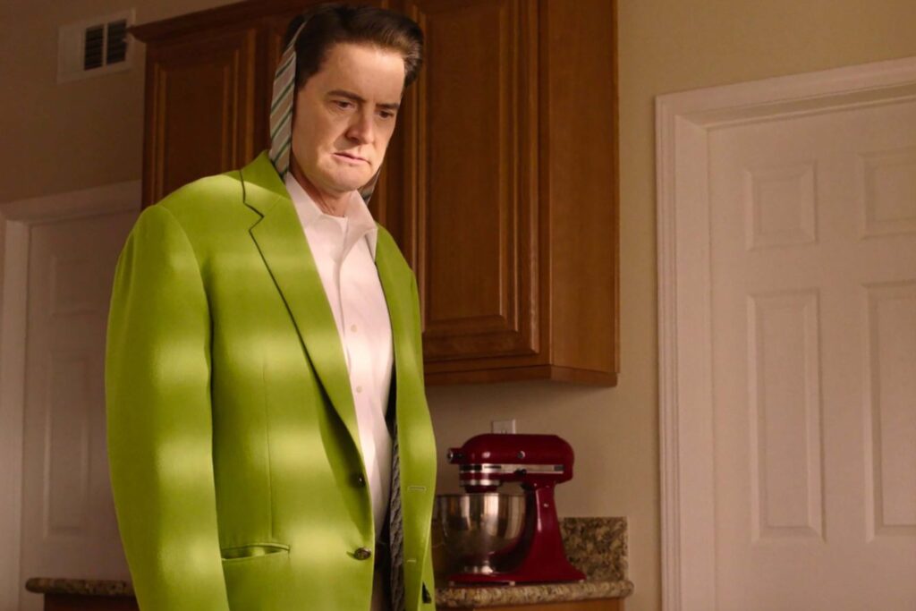 Dale Cooper, gespielt von Kyle MacLachlan, steht in einer Küche. Er trägt ein leuchtend grünes Sakko, ein weißes Hemd und eine gestreifte Krawatte, die über seinem Kopf hängt. Sonnenlicht wirft horizontale Schatten über seine Kleidung. Im Hintergrund stehen Holzschränke, eine Arbeitsplatte und eine rote Küchenmaschine. | Media Monday #780