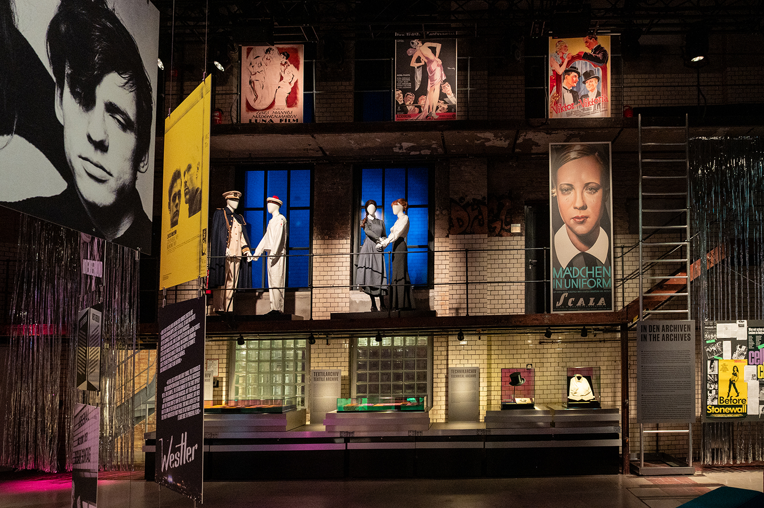 Foto der Ausstellung Inventing Queer Cinema in der Deutschen Kinemathek. Historische Kostüme und Plakate unter anderem von "Mädchen in Uniform".