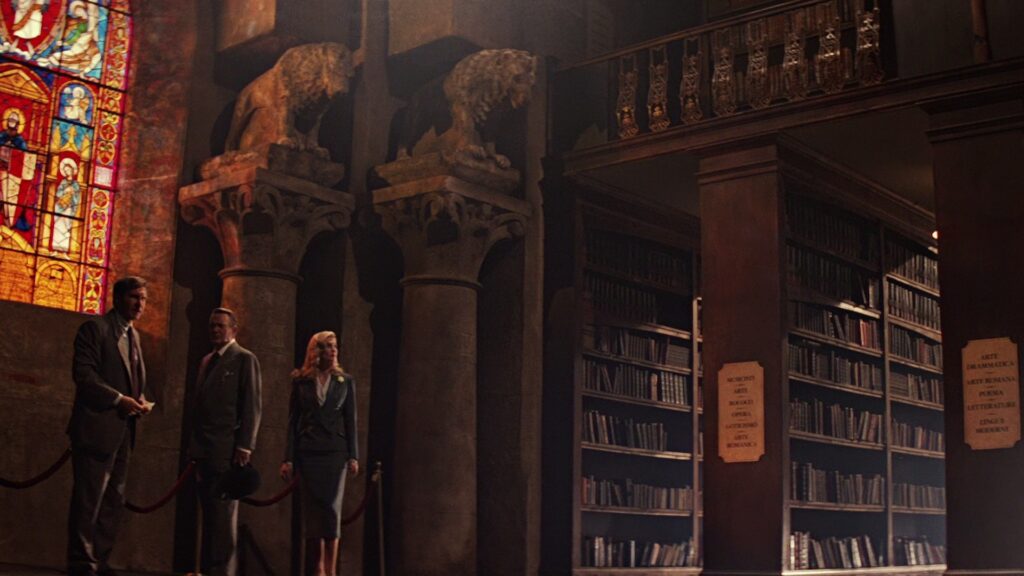Indiana Jones (Harrison Ford), Professor Henry Jones Sr. (Sean Connery) und Dr. Elsa Schneider (Alison Doody) betreten in „Indiana Jones und der letzte Kreuzzug“ die prächtige Bibliothek von Venedig. Zwischen hohen Bücherregalen, romanischen Säulen mit steinernen Löwen und einem farbenprächtigen Kirchenfenster beginnt ihre Suche nach den Hinweisen zum Heiligen Gral. | Die 5 besten Mystery-Abenteuerfilme