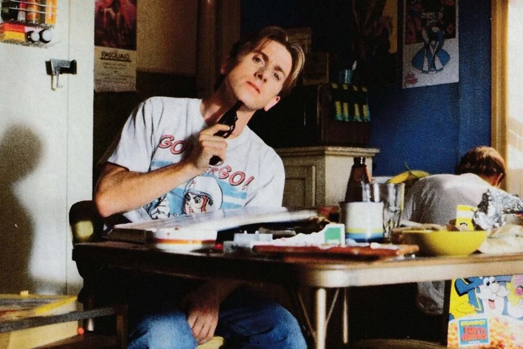Szene aus Reservoir Dogs (1992): Mr. Orange (Tim Roth) sitzt an einem überladenen Tisch in einem chaotischen Raum, sichtbar verletzt und mit einer Pistole an seinem Hals. Vor ihm liegen verstreute Alltagsgegenstände wie Papier, Geschirr und eine Müslipackung. Im Hintergrund sitzt ein weiterer Mann mit gesenktem Kopf. Die Atmosphäre wirkt angespannt und bedrückend. | Themenübersicht August 2026