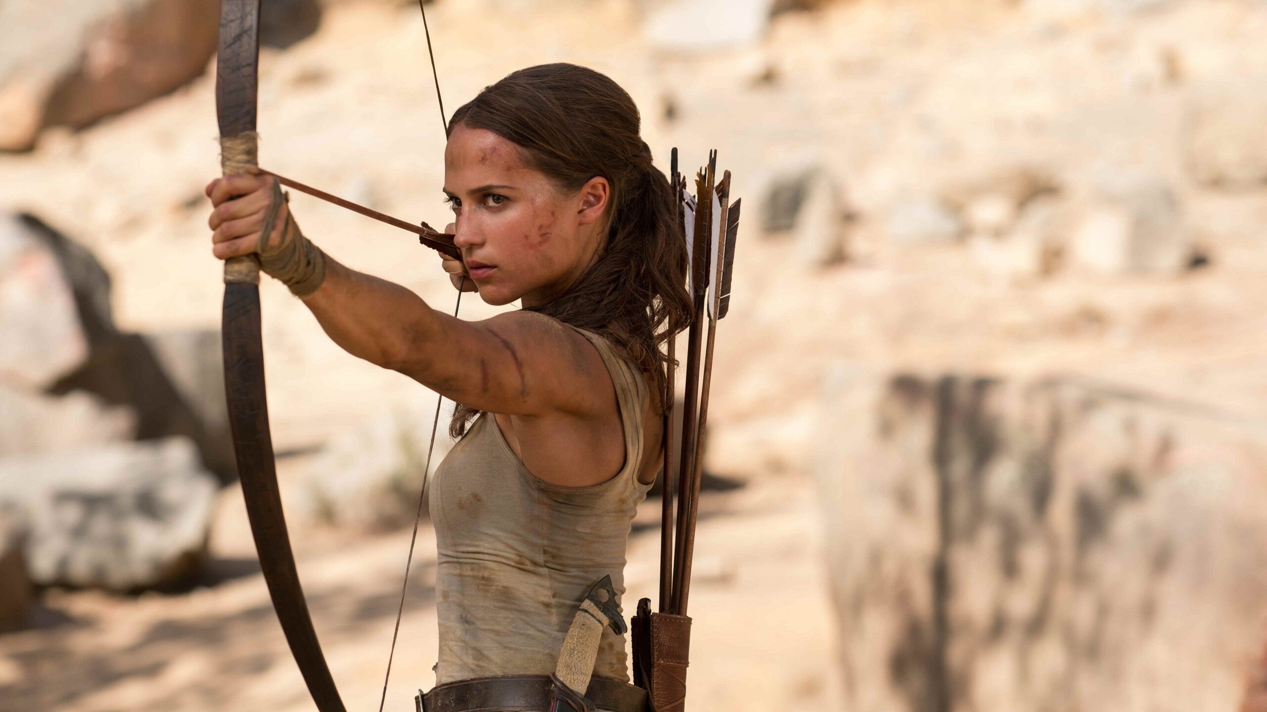 Lara Croft (Alicia Vikander) spannt in „Tomb Raider“ (2018) entschlossen ihren Bogen und nimmt ein Ziel ins Visier. Mit Pfeilköcher auf dem Rücken und sichtbaren Kampfspuren im Gesicht verkörpert sie die entschlossene Abenteurerin in der rauen Wildnis. | Die 5 besten Mystery-Abenteuerfilme