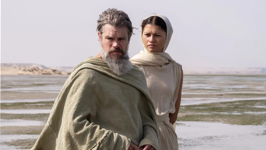 Odysseus (Matt Damon) und Athene (Zendaya) stehen am Ufer und blicken entschlossen über die weite Küstenlandschaft. Die ruhige Szene unterstreicht die mythische Atmosphäre von „Die Odyssee“ (2026).  | Die Odyssee