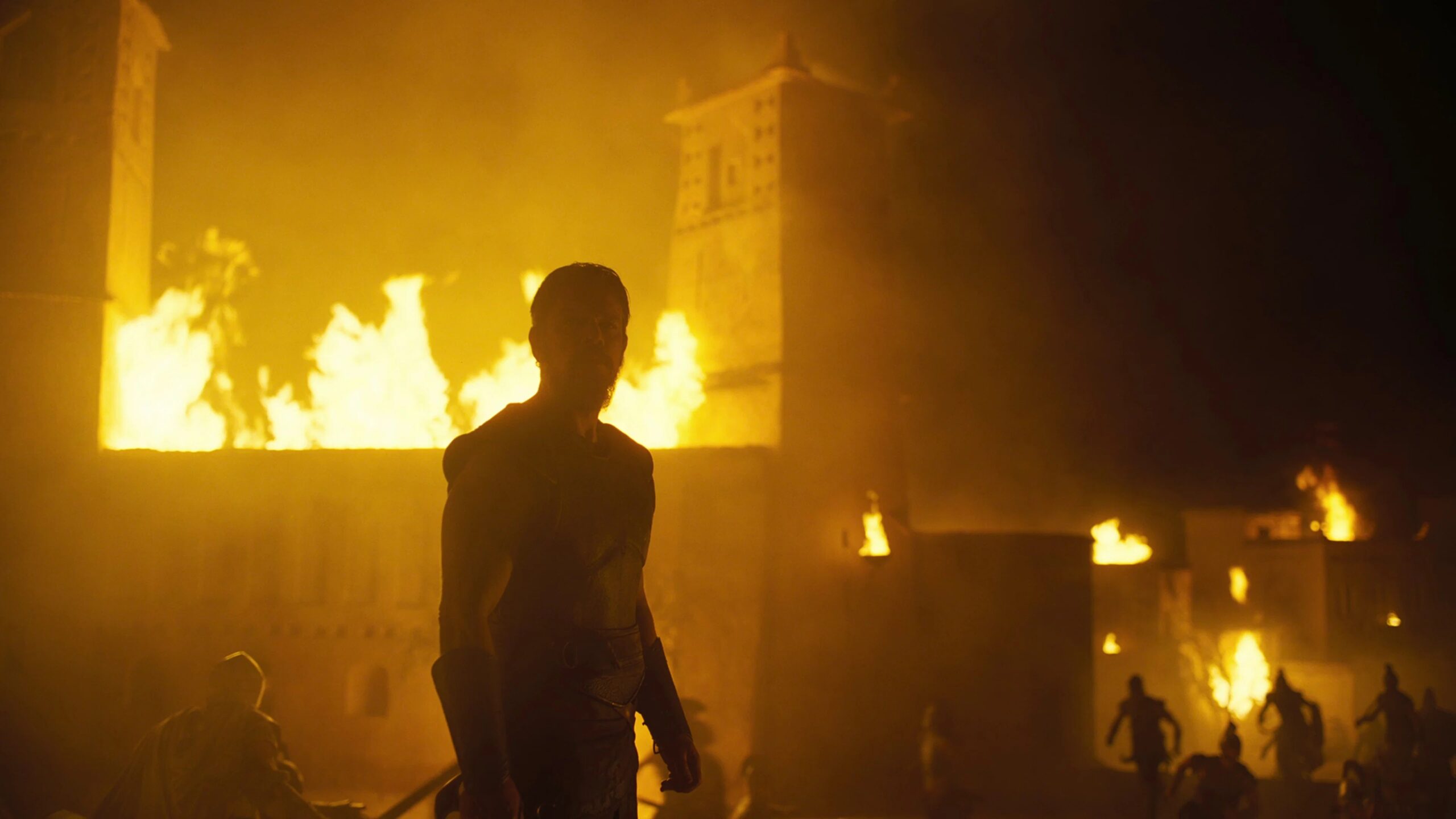 Odysseus (Matt Damon) steht vor einer brennenden Stadt, während Flammen den nächtlichen Himmel erhellen. Die Silhouette des Helden betont die zerstörerischen Folgen des Krieges.  | Die Odyssee