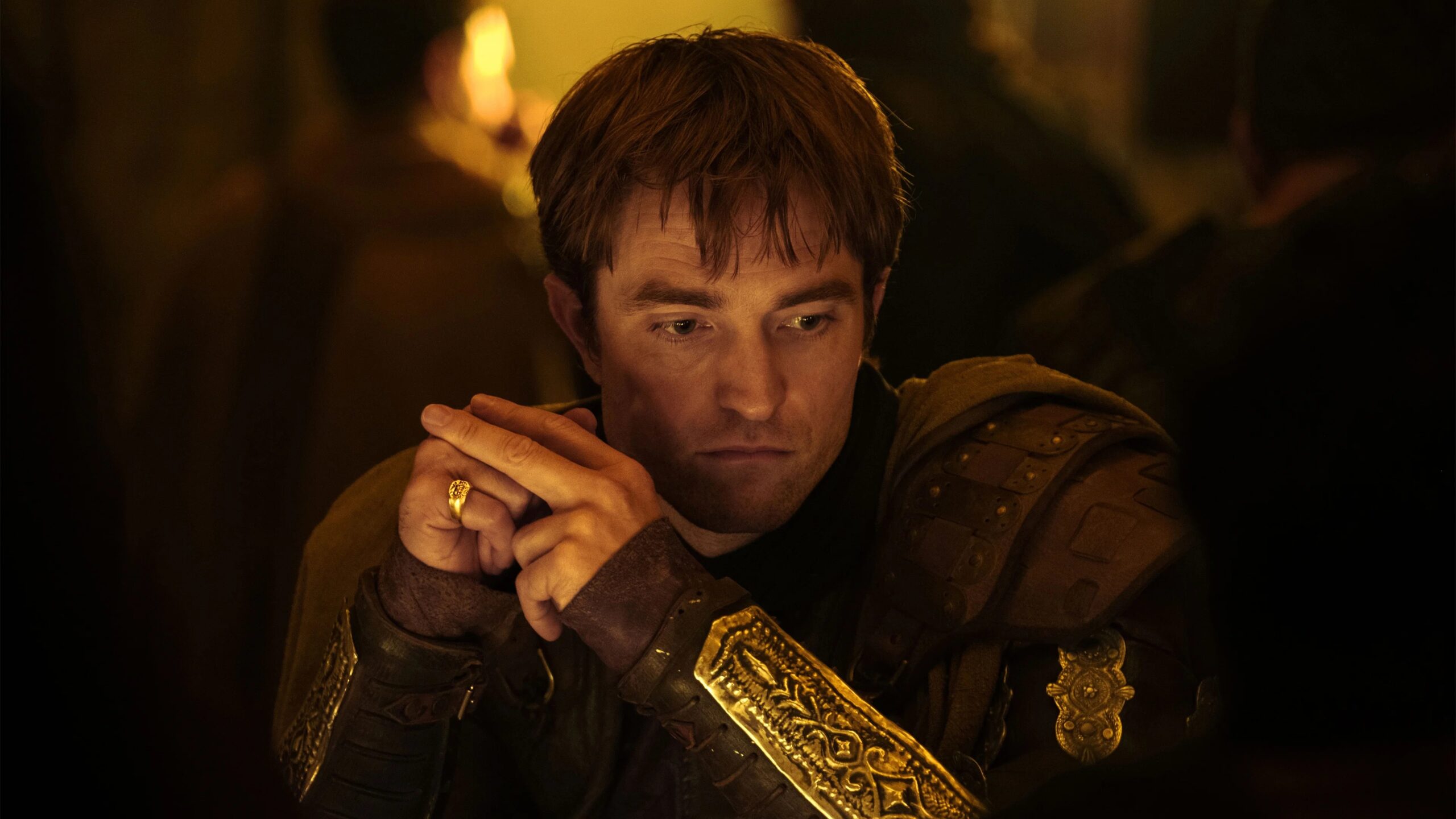 Antinoos (Robert Pattinson) sitzt nachdenklich an einer festlich gedeckten Tafel. Sein goldverzierter Harnisch erinnert an die Pracht und den Nachhall des Trojanischen Krieges.