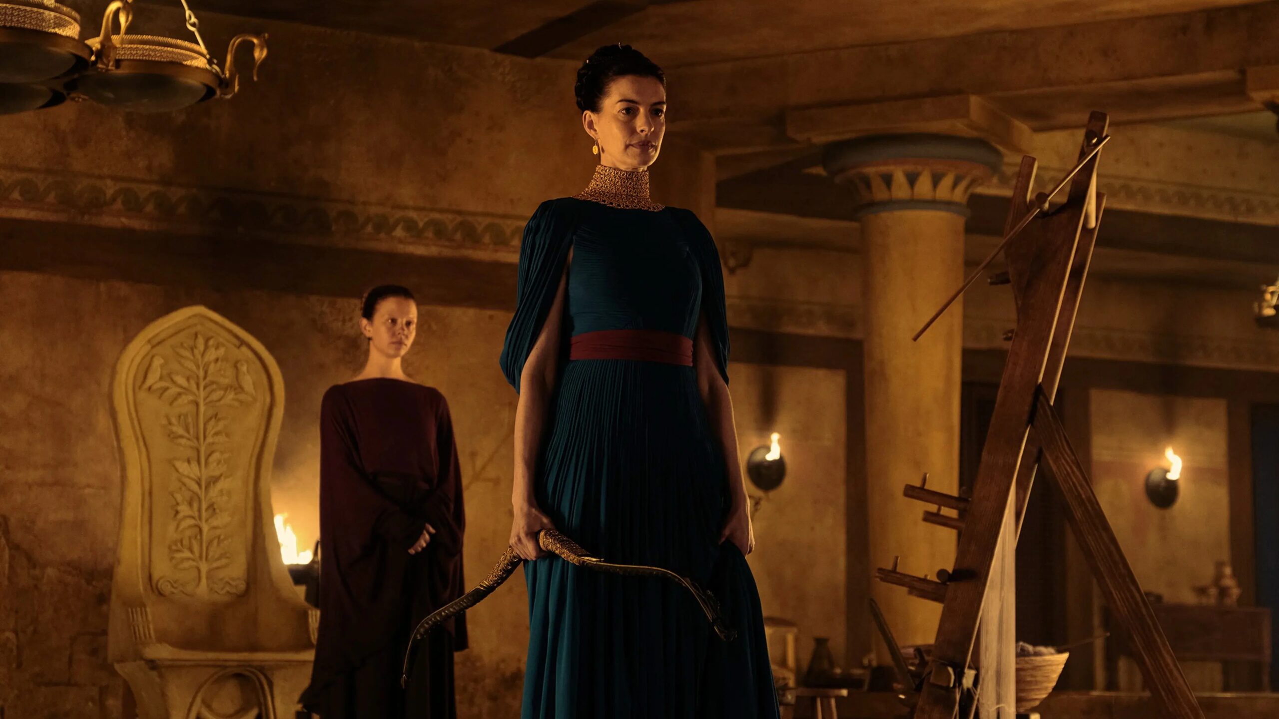 Penelope (Anne Hathaway) steht mit einem Bogen vor ihrem Webstuhl und blickt entschlossen nach vorn. Die Szene verbindet ihre Stärke mit dem berühmten Motiv des unvollendeten Gewebes.
