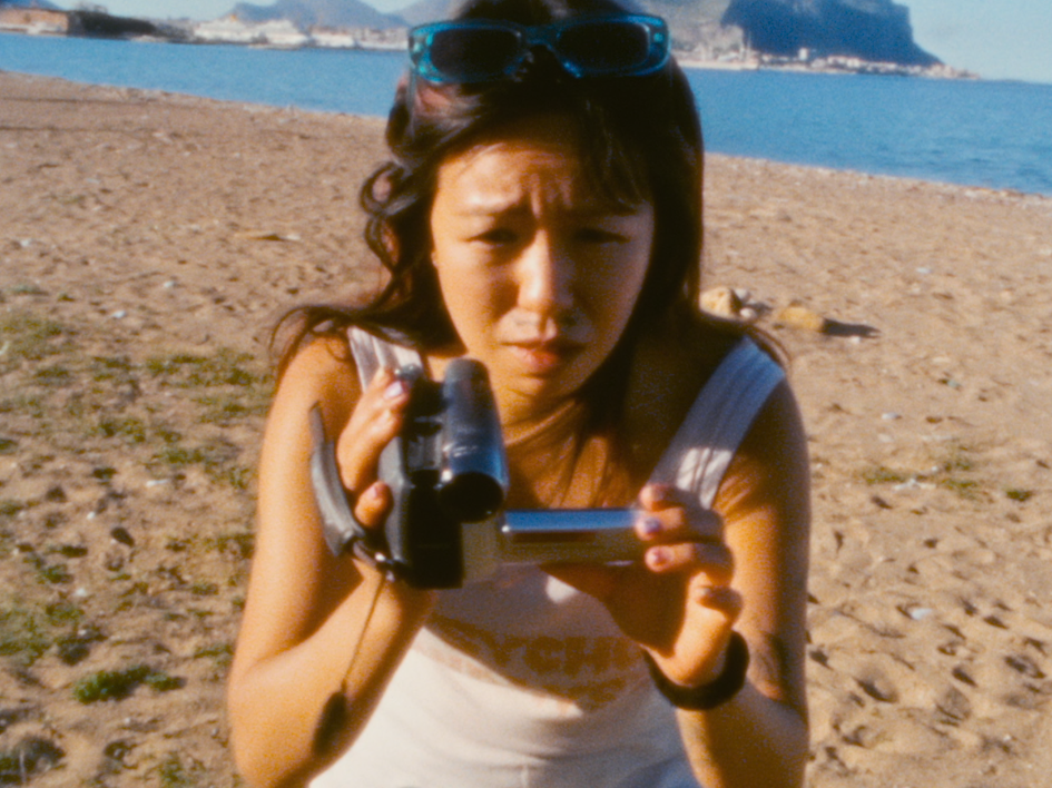 Oskar (Chang Wang) aus "Für immer 16" ist am Strand und hält eine Kamera zum Filmen in der Hand