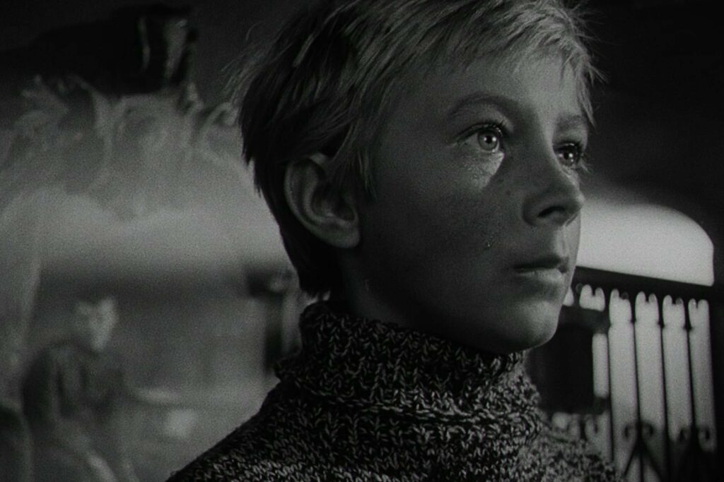 Ein schwarzweißes Porträt des Jungen Iwan, gespielt von Kolja Burljajew in Andrei Tarkovskys Film „Iwans Kindheit“ von 1962. Er blickt ernst nach vorn, trägt einen grob gestrickten, hochgeschlossenen Pullover, während der Hintergrund unscharf bleibt und eine weitere Person sowie architektonische Elemente nur angedeutet sichtbar sind. | Media Monday #788