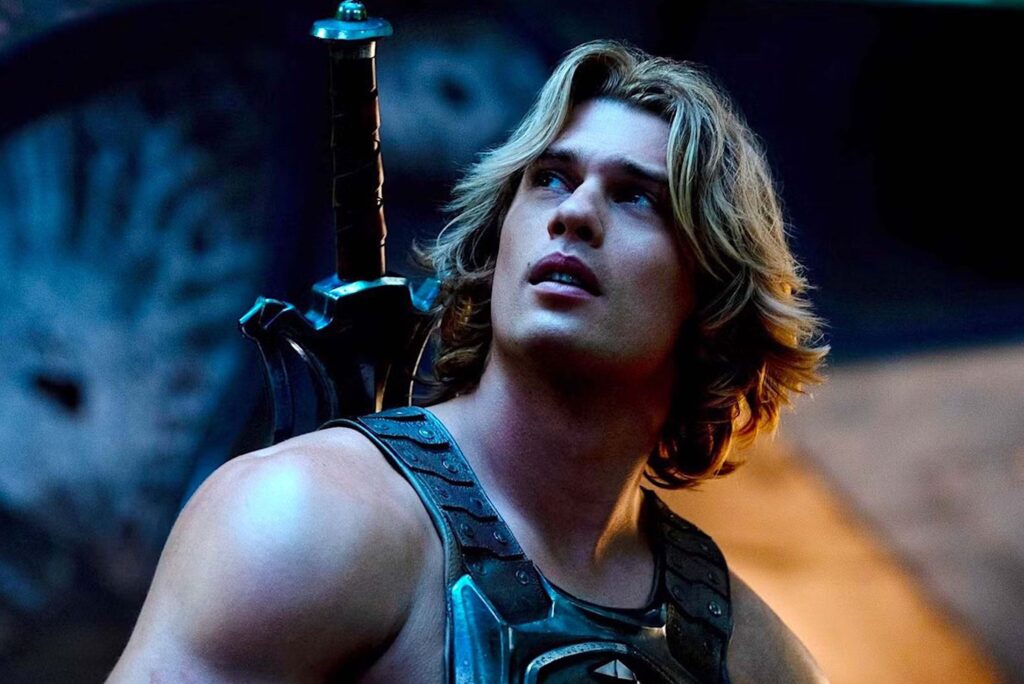 Nicholas Galitzine als He Man steht in einer dramatisch beleuchteten Szene, trägt eine metallische Brustpanzerung und hat ein großes Schwert auf dem Rücken. Blaues und orangefarbenes Licht betont sein Gesicht und die Rüstung, während der dunkle Hintergrund eine kraftvolle, heroische Atmosphäre erzeugt. | Media Monday #790