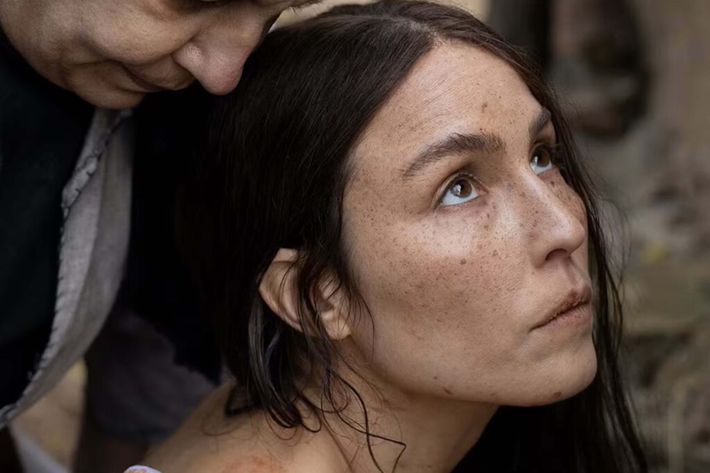 Noomi Rapace in einer Nahaufnahme aus Goran Stolevskis Film „You Won’t Be Alone“ von 2022. Sie blickt ernst nach oben, ihr Gesicht ist von natürlichem Licht betont, während eine weitere Person dicht hinter ihr steht. Der Hintergrund ist unscharf und deutet eine Außenumgebung an. | Media Monday #788