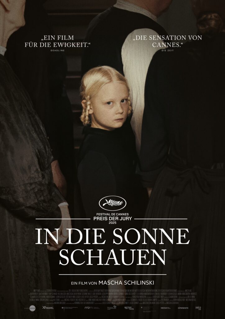 Das Bild zeigt die junge Alma (Hanna Heckt) zwischen ihren Verwandten während der Trauerandacht stehen. Das Bild zeigt die düstere Seite des Films "In die Sonne schauen" sehr atmosphärisch und deutlich