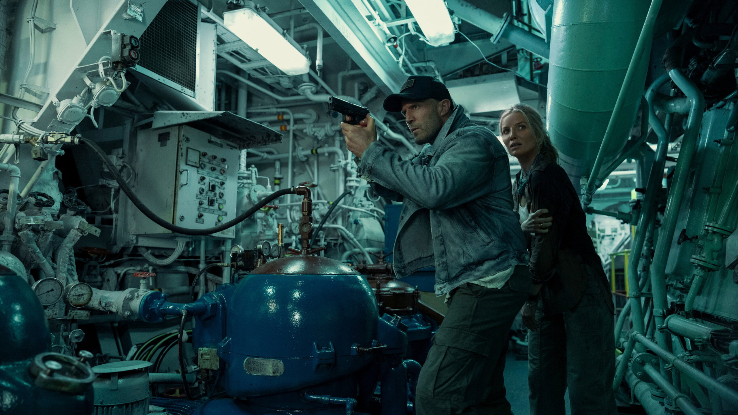 Das Bild zeigt Jason Stathman mit einer Pistole gemeinsam mit Annabelle Wallis in einem Maschinenraum in einer Szene des Films Mutiny.