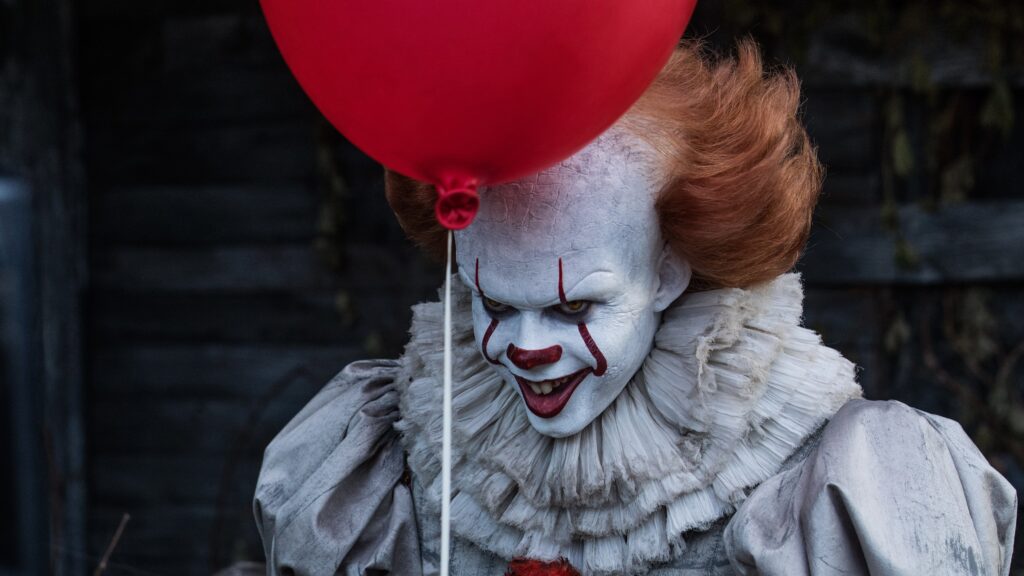 Der Clown Pennywise (Bill Skarsgård) hält einen roten Ballon und lächelt böse in die Kamera.