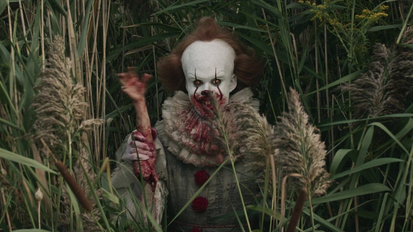 Pennywise (Bill Skarsgård) lächelt und winkt mit einem abgetrennten Arm eines Opfers.