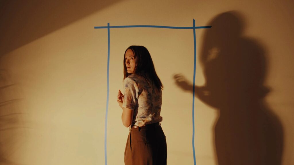 Das Bild zeigt die weibliche Hauptfigur vor einer Wand stehen auf die ein Türrahmen mit Kleber dargestellt ist — Backrooms | 2026© Constantin Film Distribution