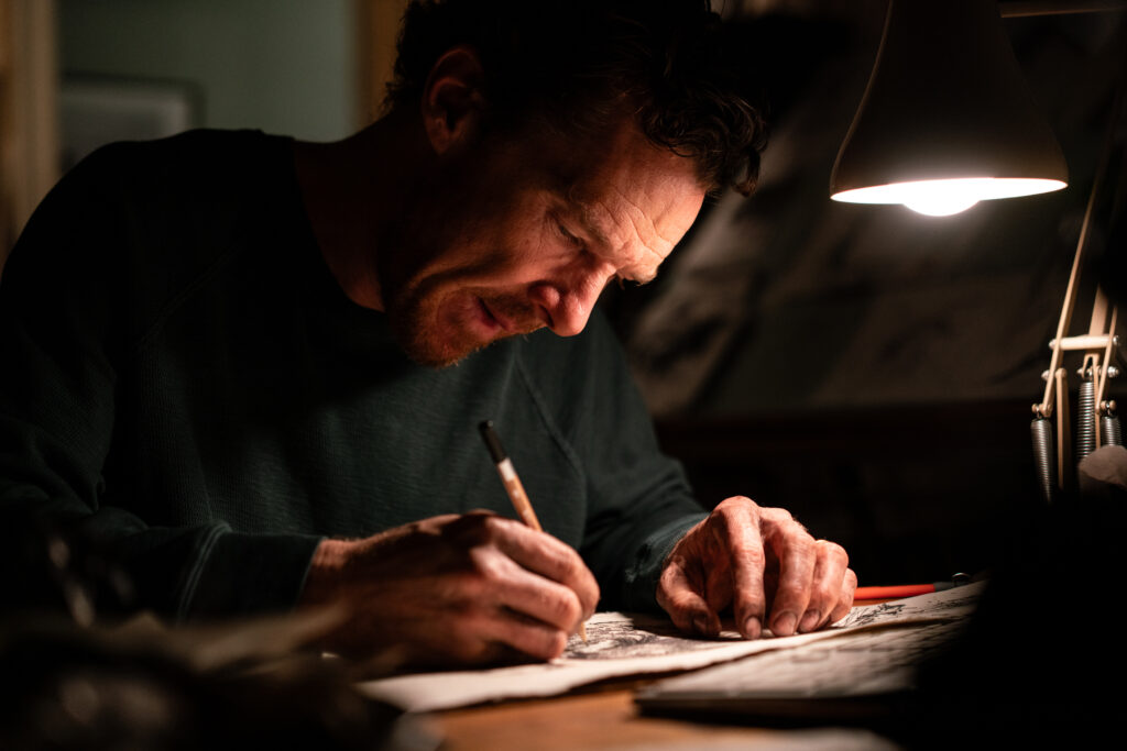 Das Bild zeigt Benedict Cumberbatch am Schreibtisch. Er fertigt gerade eine Zeichnung an | Das Ding mit Federn