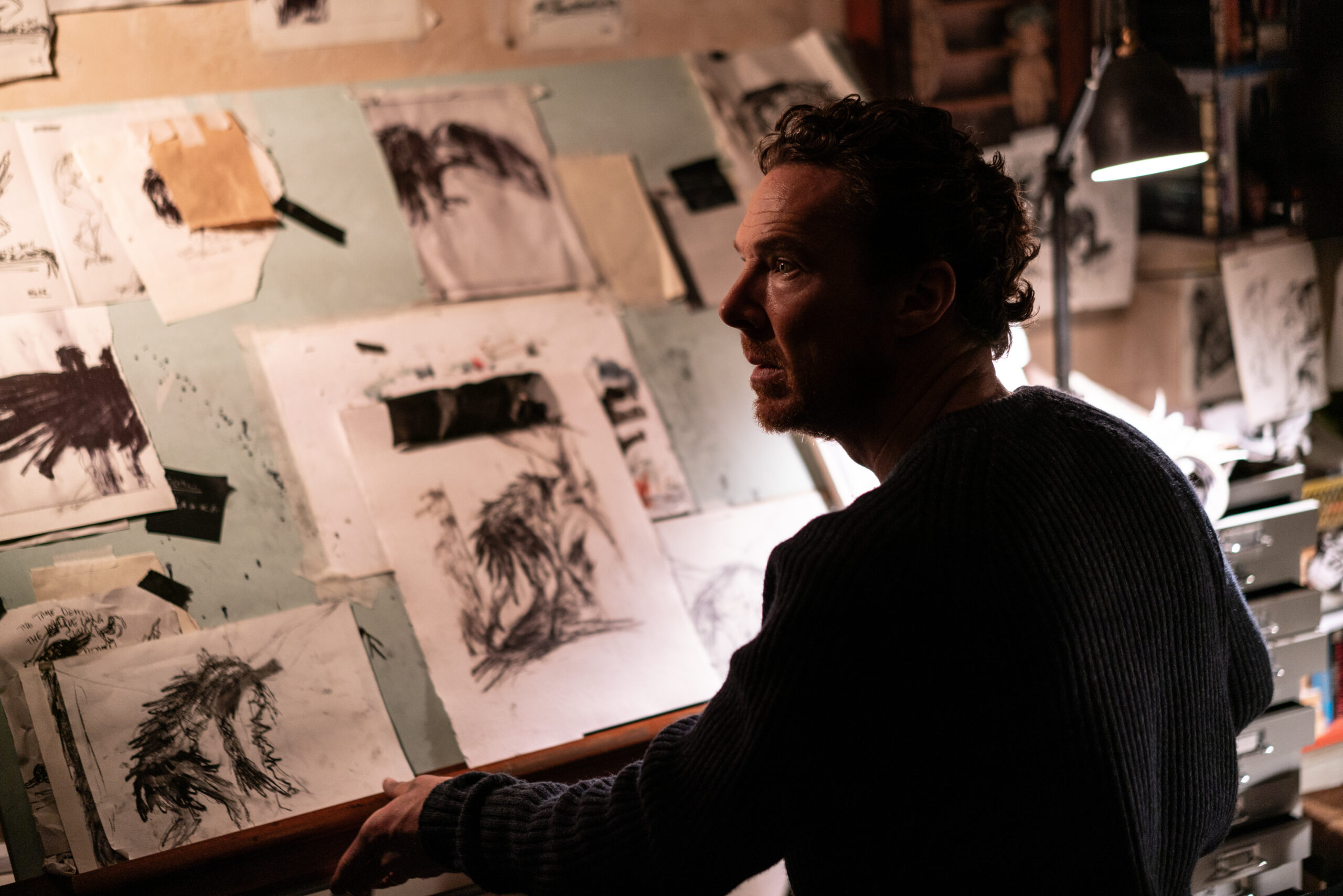 Das Bild zeigt Benedict Cumberbatch in "Das Ding mit Federn" am Malpult. Vor ihm sind schwarze Skizzen auf weißem Papier zu sehen. Überwiegend mit Kohle gemalt